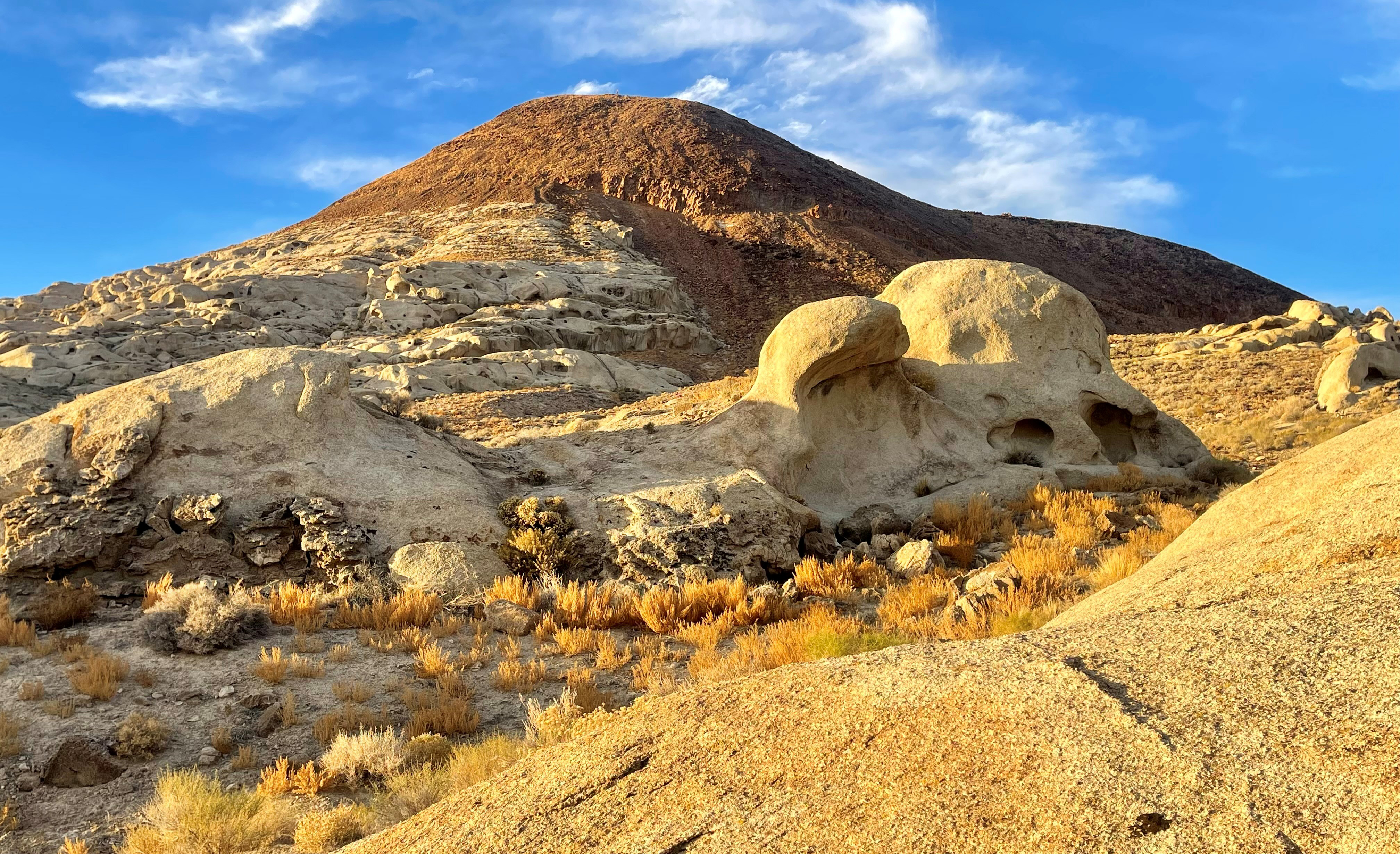 Desert landscape of orange and white rocks in golden light from the sun with a bright blue sky.