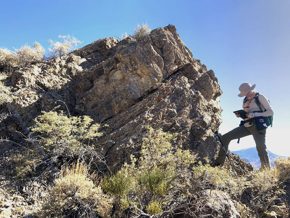 Geologic mapper stands next to rock grouping looking at mapping device.