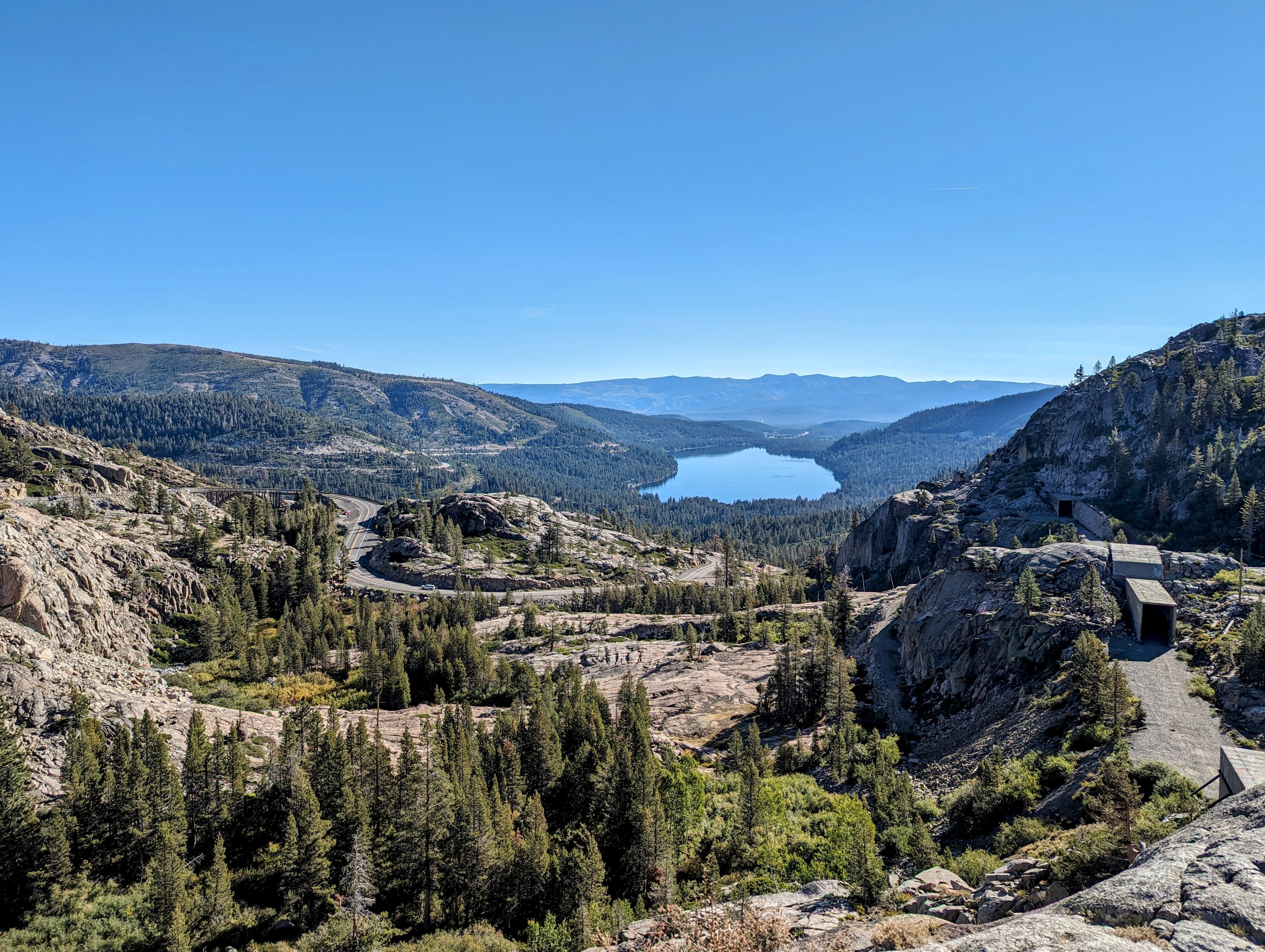 Expansive view over tree covered slopes towards a blue lake in the distance.